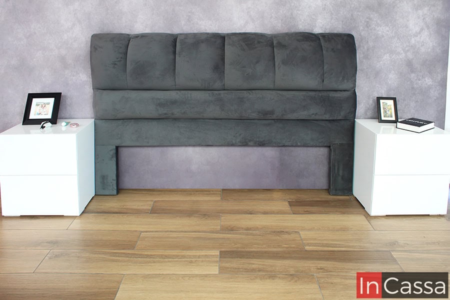 Se presenta la estructura de la cabecera tapizada en suede gris oxford sin la base, lo que permite visualizar su tamaño imponente y su estilo moderno. Los cojines acolchonados ofrecen un soporte cómodo y decorativo.
