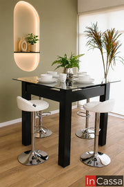 Se aprecia el Comedor Alto Modelo CABRERA para 4 personas en color chocolate con cubierta de cristal y bancos neumáticos tapizados en tacto piel color blanco. Su diseño elevado de estilo contemporáneo aporta elegancia y funcionalidad, siendo ideal para cocinas, barras o espacios modernos donde se busca comodidad y un ambiente sofisticado.