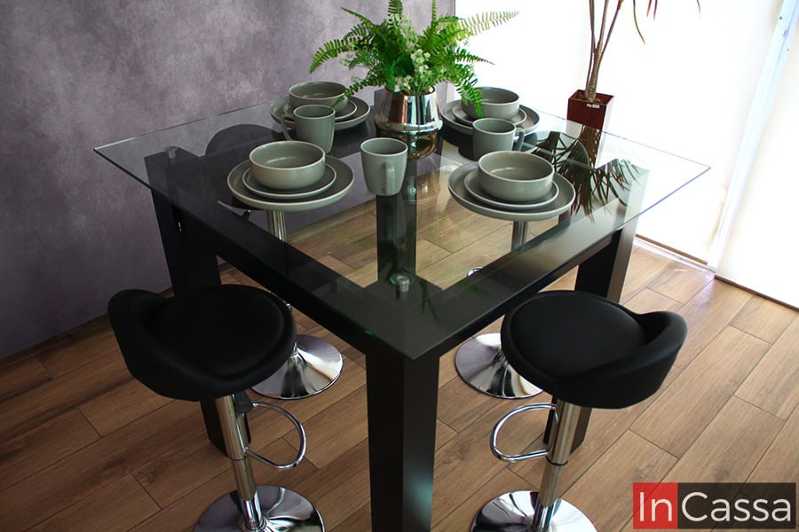 Una fotografía desde una toma superior del comedor chocolate, en la que se destaca la cubierta de cristal suspendida de la mesa así como los asientos de tacto piel negro de los bancos neumáticos.