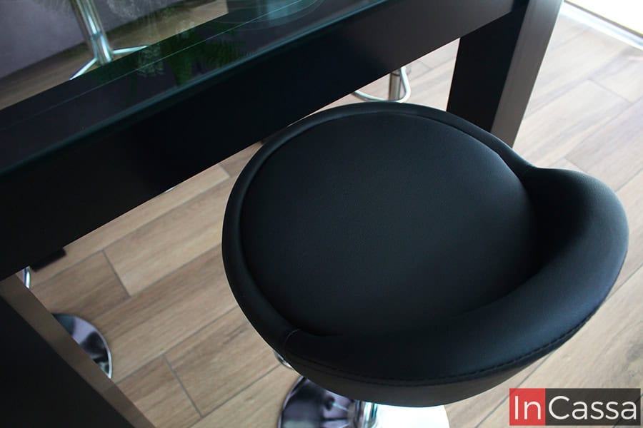 La imagen se concentra en el asiento de uno de los bancos neumáticos, el cual se encuentra totalmente tapizado en tacto piel negro. El asiento tiene una forma circular con un respaldo pequeño.