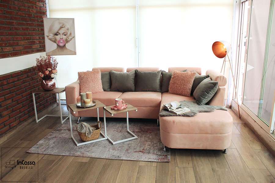 Sala Esquinera moderna en suede rosa y cojines grises, decorada con mesa auxiliar, lámpara vintage y cuadro pop art. Perfecta para interiores contemporáneos y espacios acogedores.