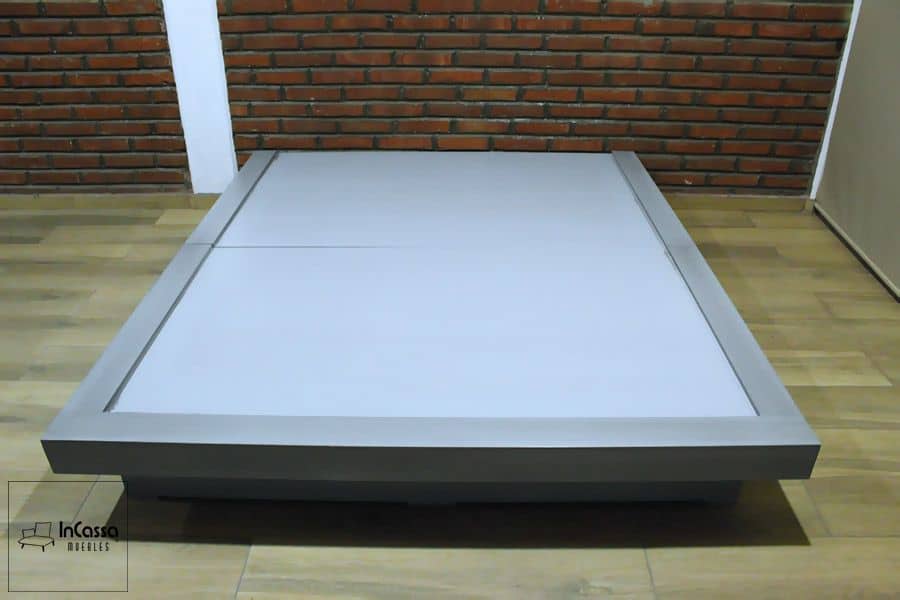 La imagen muestra una base de cama en color gris cenizo claro con un diseño moderno de perfil bajo y bordes elevados. Su estructura robusta y elegante proporciona estabilidad, fusionando funcionalidad y estilo contemporáneo para cualquier dormitorio.