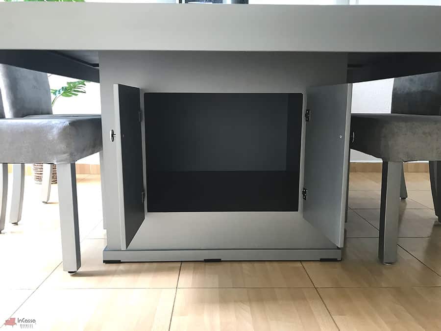 La imagen muestra el gabinete inferior de la mesa Cambridge para ocho personas, con ambas puertas abiertas, mostrando su acabado silver completo. Este práctico compartimento central ofrece espacio adicional para almacenar objetos de uso cotidiano.