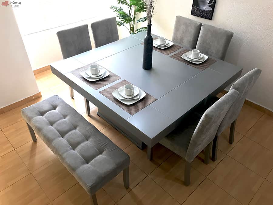Una toma superior del comedor Cambridge muestra su distribución para 8 personas: cuatro sillas en los costados, dos en cabecera y una banca, todas tapizadas en suede gris perla. La mesa cuadrada en tono silver completo destaca por su amplitud y diseño contemporáneo.