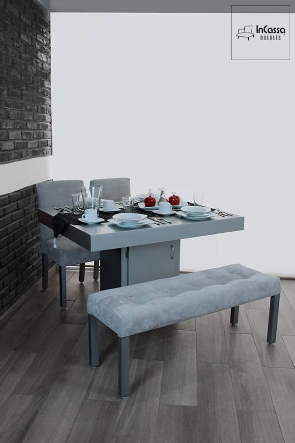 La imagen muestra el comedor Cambridge para 4 personas en tono silver, con mesa de base central tipo gabinete, sillas tapizadas en tacto suave y una banca con acabado capitonado. Ideal para espacios modernos y elegantes.