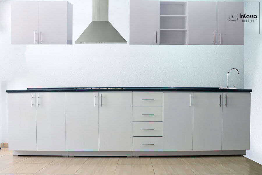 Esta fotografía muestra la cocina integral en una toma frontal que permite apreciar el diseño lineal del modelo, en color blanco con cubierta de formaica estilo mármol negro. Destaca la distribución simétrica de las puertas con jaladeras metálicas alargadas, así como los módulos superiores con puertas lisas, entrepaños abiertos y espacio para campana. Ideal para cocinas modernas y funcionales.