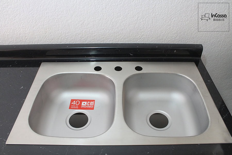 En esta foto se presenta una toma central de la tarja doble fabricada en acero inoxidable con acabado satinado. Se encuentra empotrada en una elegante cubierta de formaica en acabado mármol negro, que aporta un contraste moderno. El diseño incluye tres perforaciones para instalación de mezcladora y accesorios, ideal para una cocina funcional y estilizada.