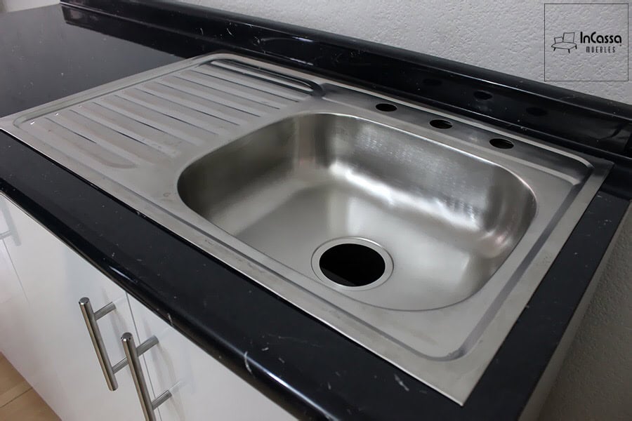 Se observa un acercamiento al área de lavado de la Cocina integral CANADÁ de 3.30 m para ESTUFA en color blanco, donde la cubierta de formaica en estilo mármol negro resalta por su elegante contraste con la tarja de acero inoxidable. Esta combinación ofrece una superficie resistente, de fácil limpieza y con un diseño contemporáneo que aporta funcionalidad y un acabado sofisticado al espacio de trabajo diario.