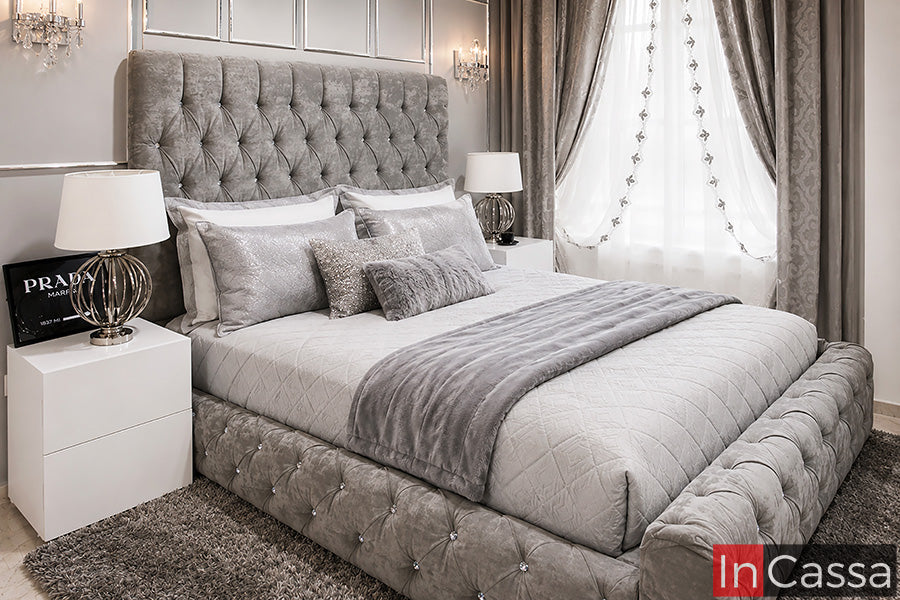 Recámara tapizada capitoné Modelo CARTIER en suede gris perla, con cabecera alta y base acolchada decoradas con capitonado profundo y detalles tipo cristal. Los burós blancos crean un contraste elegante con el tapizado gris, dando al conjunto un estilo sofisticado y contemporáneo.
