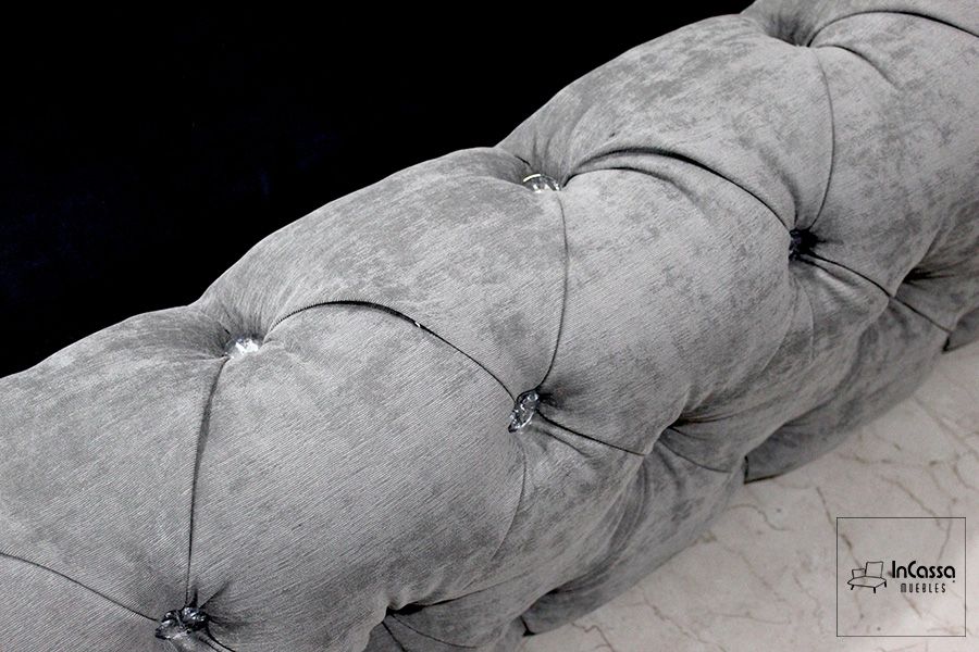 La foto se concentra en uno de los bordes laterales de la base, permitiendo apreciar más de cerca la textura de la tela suede color gris perla y los botones con forma de diamante utilizado para el capitoneado.