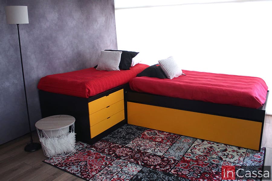 Trilitera infantil de color chocolate con cajones y base oculta en color amarillo, instalada en una habitación con pared gris y ventana completa decorada con una gran tapete de tonos rojizos.