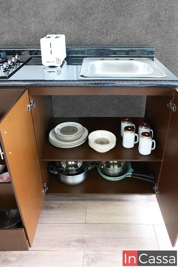 En la parte inferior de la cocina se observa un compartimento abierto en color tabaco completo donde se almacenan platos y ollas, aprovechando al máximo el espacio de la cocina.