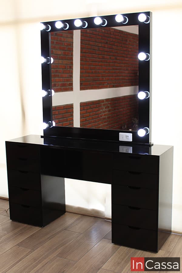 La toma proporciona una imagen completa del tocador, en la que podemos ver detalladamente la construcción de la mesa así como el grosor del marco del espejo, además también es posible apreciar el brillo de sus 12 focos LED y el acabado negro brillante presente en todo el tocador.