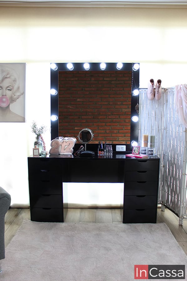 Tocador tamaño jumbo en color negro con acabado brillante, el tocador incluye un espejo en su diseño con 12 focos LED integrados en el marco, mismo que mantiene el color chocolate. El mueble es presentado frente a una ventana de pantalla completa con cortina.