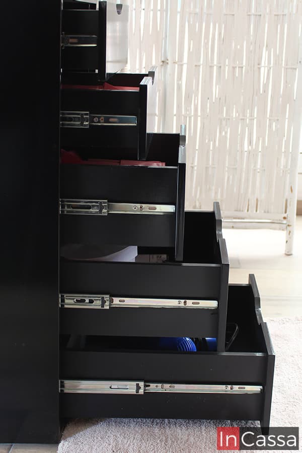 La imagen muestra una toma lateral del mueble, en la que se muestra los cajones abiertos destacando principalmente sus sistema de apertura y cierre guiado por rieles metálicos, además es posible ver que los cajones conservan el mismo color negro presente en la totalidad del tocador.