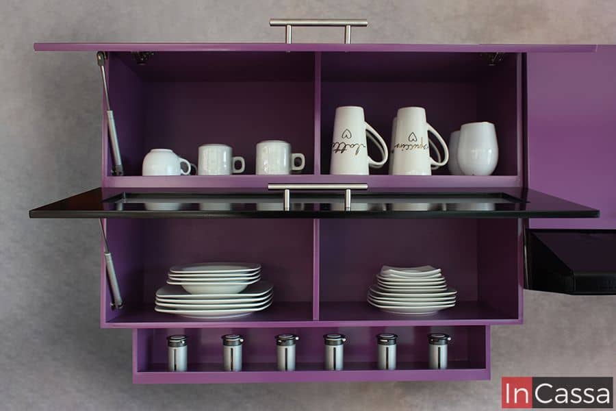 La imagen muestra un alacena superior en color uva completo, con compartimentos organizados en los que pueden apreciarse tazas, platos y especieros en la parte inferior. Además de pistones neumáticos en las puertas para su apertura y cierre vertical. Ideal para mantener la cocina ordenada y funcional.