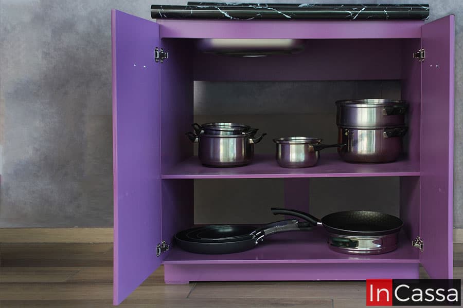 La imagen presenta el módulo de tarja de la cocina con sus dos puertas abiertas mostrando su interior, el cuál cuenta con dos amplios compartimentos divididos por un entrepaño horizontal, todas las partes interiores son de color uva al igual que la estructura exterior del mueble. El módulo además conserva espacios libres en su parte trasera para la instalación de la plomería.