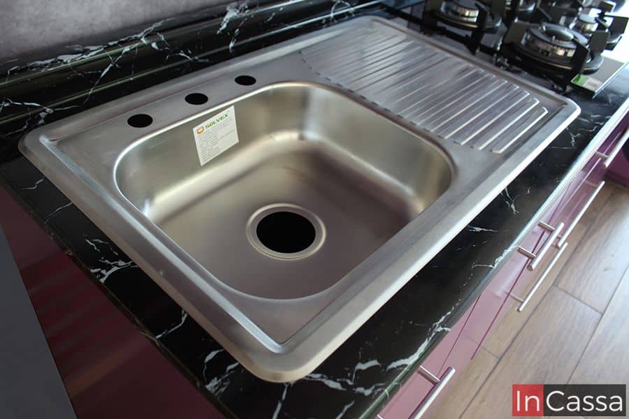 Foto de la tarja de acero inoxidable integrada en la cubierta de formaica en estilo mármol negro de la cocina, combina elegancia y funcionalidad. Su diseño con un área para escurrir platos ofrece practicidad en la cocina, complementando el estilo moderno del conjunto.