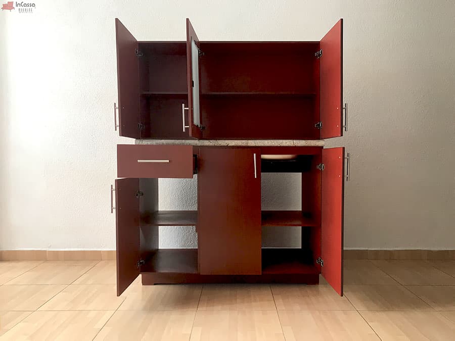 Se presenta el módulo inferior y superior de la cocina en color maple oscuro con todas sus puertas abiertas, revelando los amplios compartimentos con entrepaños interiores, un cajón funcional y espacio para tarja bajo cubierta de formaica.