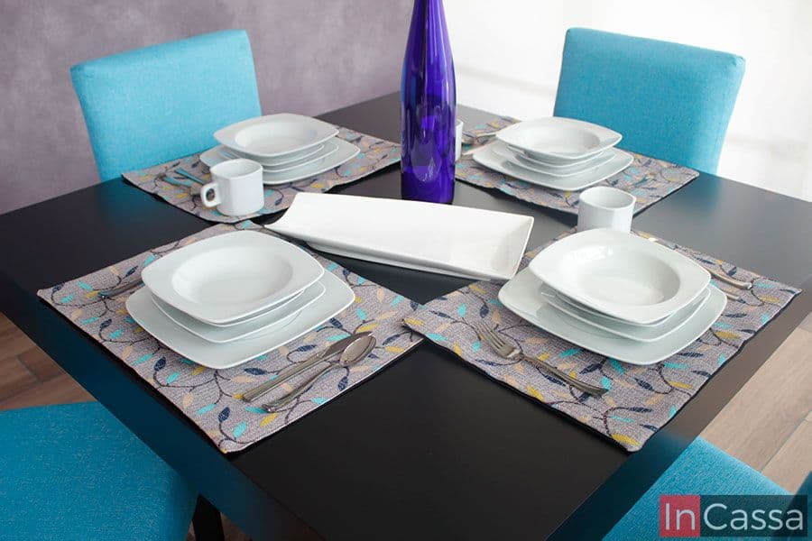 La imagen permite concentrarnos mayormente en la cubierta de la mesa la cual es adornada por diferentes tipos de vajillas y utensilios, los cuales nos permiten hacernos una idea de su longitud además de que resaltan la pintura color chocolate de la mesa así como su acabado mate. Igualmente podemos observar los respaldos de las cuatro sillas tapizadas en pliana aqua que acompañan la mesa.