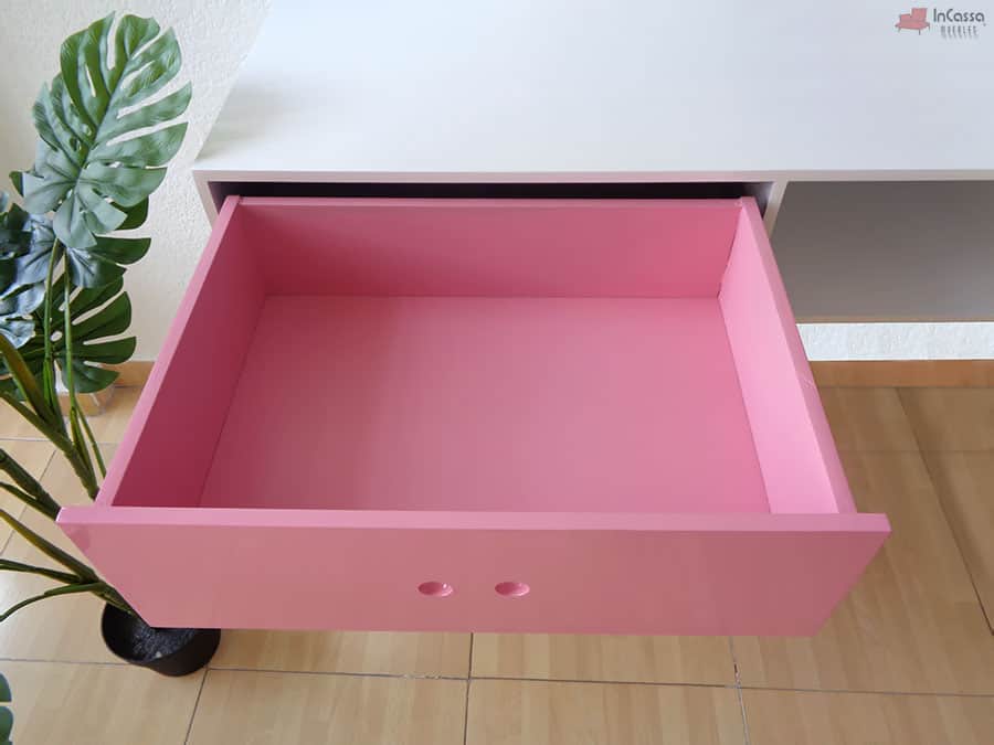 La imagen muestra el cajón del escritorio en color rosa completamente extendido, revelando su interior espacioso y acabado uniforme. Su diseño minimalista incluye perforaciones como tiradores, combinando estética y funcionalidad para organizar objetos con facilidad.