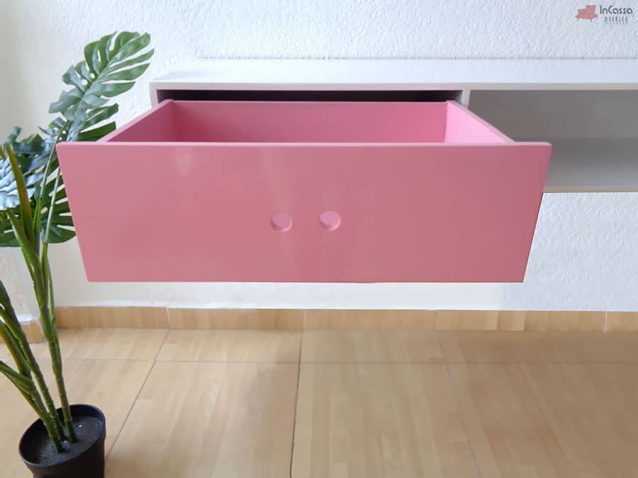 Se presenta el cajón del escritorio en acabado rosa completamente abierto, resaltando su diseño minimalista con perforaciones como tiradores. Su estructura espaciosa y resistente permite almacenar diversos objetos, combinando funcionalidad y estilo en este moderno escritorio flotante.