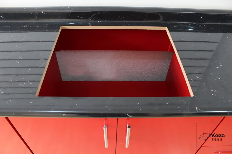 La imagen muestra el espacio dedicado a la estufa empotrable, integrado en la cubierta de formaica en estilo mármol negro, ideal para una estética moderna y funcional.