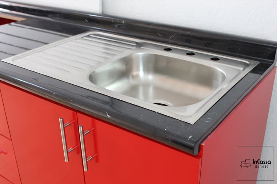 Una toma de la tarja de acero inoxidable con escurridor, perfecta para el uso diario, ubicada en una cubierta de formaica en estilo mármol negro que facilita la limpieza y aporta elegancia.