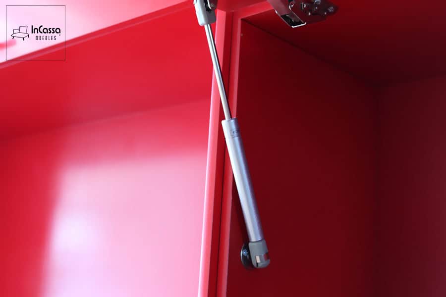 Una toma de los pistones que sostienen las puertas de las alacenas superiores rojas completas, brindando seguridad y un cierre suave y silencioso en cada apertura.