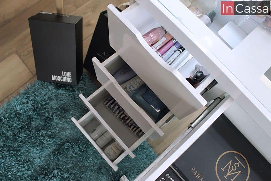 Una imagen que nos muestra detalladamente el interior de los cajones incorporados en el tocador, donde cada uno cuenta con diferentes tipos de utensilios que además de funcionar como decoración para la toma también ejemplifican la capacidad en cada cajón. Su diseño, enteramente en tono blanco al igual que la estructura del tocador, tiene un pequeño hueco en el borde superior lo que hace posible abrir y cerrar cada cajón sin necesidad de jaladeras.