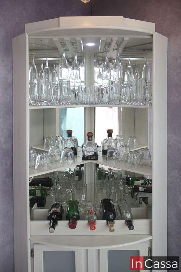 Este mueble de bar de color blanco combina funcionalidad y estilo. Su diseño incluye estantes de vidrio con soportes para copas invertidas, una iluminación LED sutil y un espejo que acentúa la profundidad y el orden en la disposición de botellas y vasos. Los compartimentos inferiores, ideales para almacenar botellas, complementan su estructura elegante y práctica.