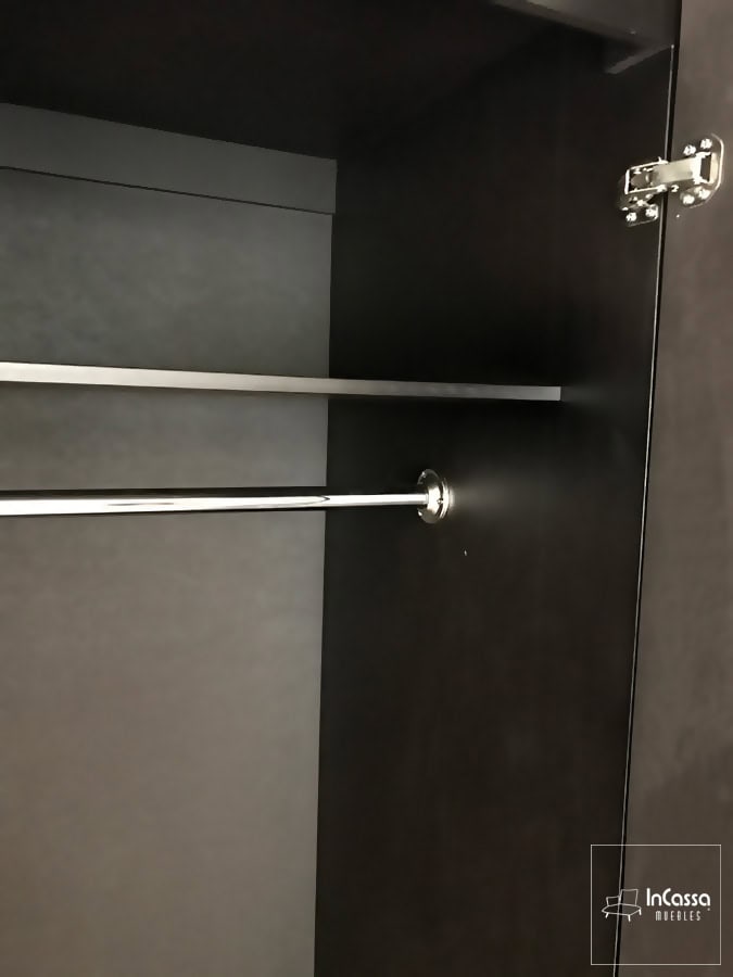 Está toma se concentra en una de las barras metálicas incorporadas al clóset para colgar ropa. Está es metálica con un acabado cromado, y se encuentra instalada debajo de un entrepaño que añade un compartimento extra al espacio, mismo que tiene un tono chocolate en su totalidad al igual que el resto del mueble.