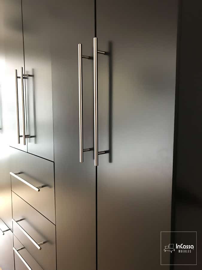 En esta foto vemos una toma lateral cercana del clóset chocolate, en la que destacan sus jaladeras metálicas integradas a cada puerta y cajón del mueble. Siendo de estilo barra T, las jaladeras además son un complemento que añade sofisticación al diseño moderno del clóset.