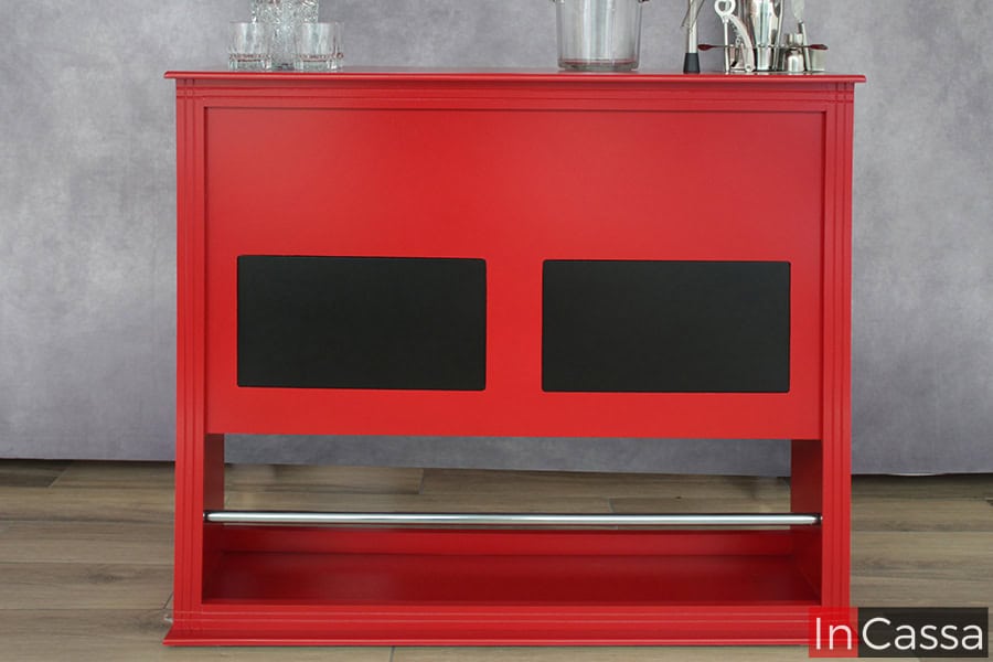 Barra cantina minimalista de color rojo con parches decorativos en color negro y una barra posa pies metálica, instalada junto a una pared gris.