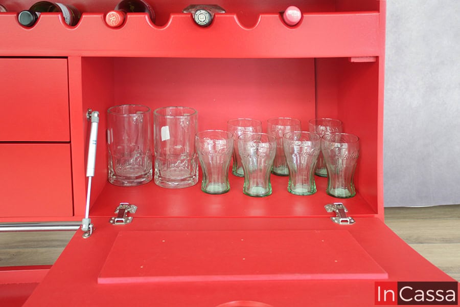 Está imagen nos enseña el interior del compartimento incluido en la parte trasera de la cantina, como con el resto del mueble esta parte es de color rojo en su totalidad; además vemos un pistón neumático incorporado para apertura y cierre de la puerta del compartimento.