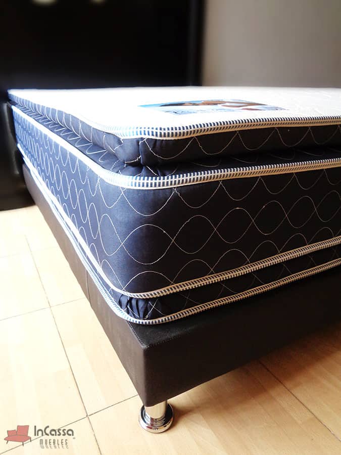 Colchón de doble colchoneta apoyado en una base con tapiz chocolate, el acolchonado del colchón es hueso y los bordes de tono azulado.