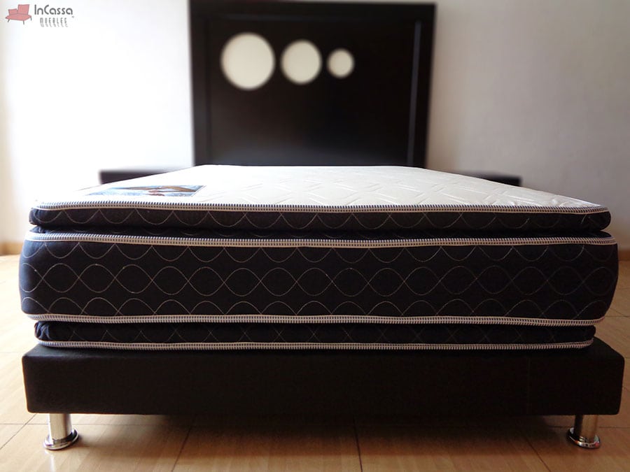 Una foto frontal del colchón, en la que la doble colchoneta del modelo se hace mucho más notable, además de que se nos ofrece una mejor vista de la base y la cabecera de la recámara chocolate en la que se presenta el colchón.