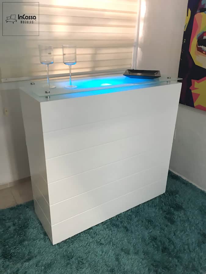Una toma angular muestra una cantina blanca de líneas horizontales con cubierta de cristal templado. La iluminación LED en azul crea un efecto visual moderno y vibrante, ideal para destacar en espacios contemporáneos.