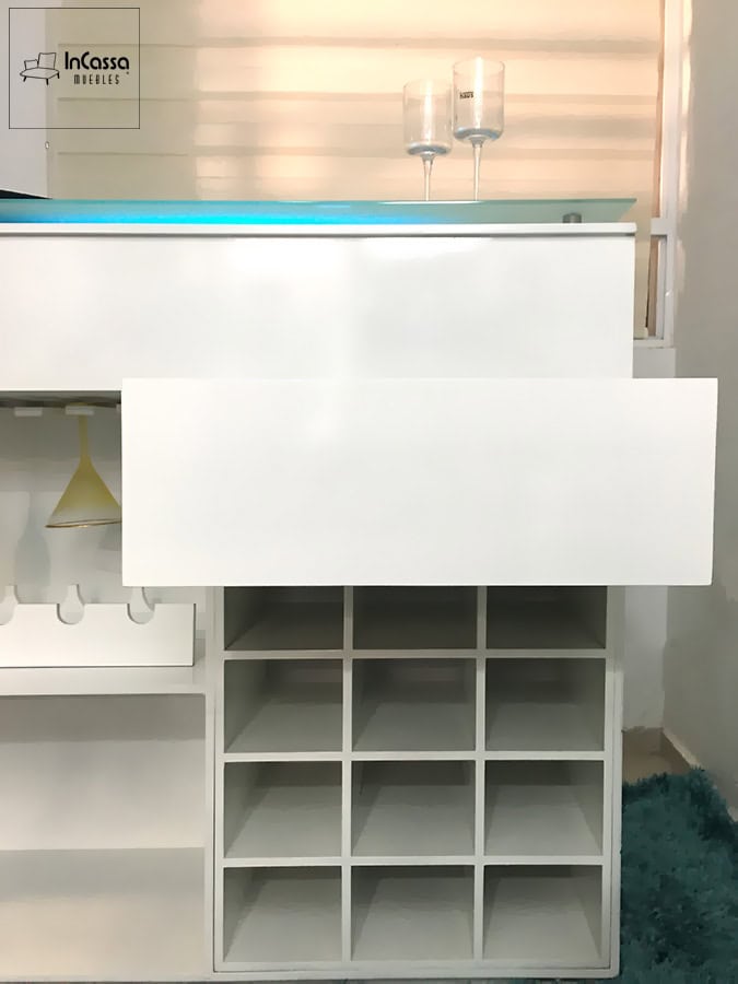 La imagen muestra una vista frontal de la cantina blanca con el cajón principal extendido. A la derecha, se aprecia un módulo con divisiones para múltiples botellas, ideal para mantener el orden. El diseño combina funcionalidad y estilo moderno.