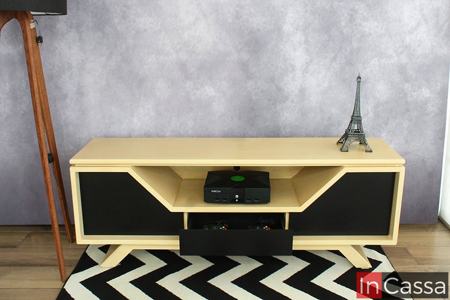 La foto presenta el mueble de TV modelo Escandinavia en ángulo frontal, elaborado en MDF con acabado natural y frentes en chocolate mate. Se aprecia su cajón central abierto para almacenamiento, junto con repisas y laterales cerrados, combinando estética moderna y practicidad.