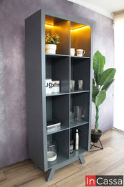 La imagen muestra una vitrina minimalista en color gris oxford con diseño vertical y estructura limpia, equipada con iluminación LED cálida en la parte superior que realza cada compartimento, ideal para exhibir cristalería y decoración con un toque moderno y elegante.