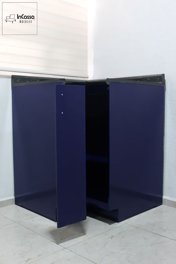 Imagen del módulo esquinero de cocina Italia en color azul marino brillante, con cubierta de formaica tipo mármol negro y puerta parcialmente abierta que revela su interior espacioso con repisa central. La toma frontal muestra su practicidad para almacenamiento y su acabado moderno.