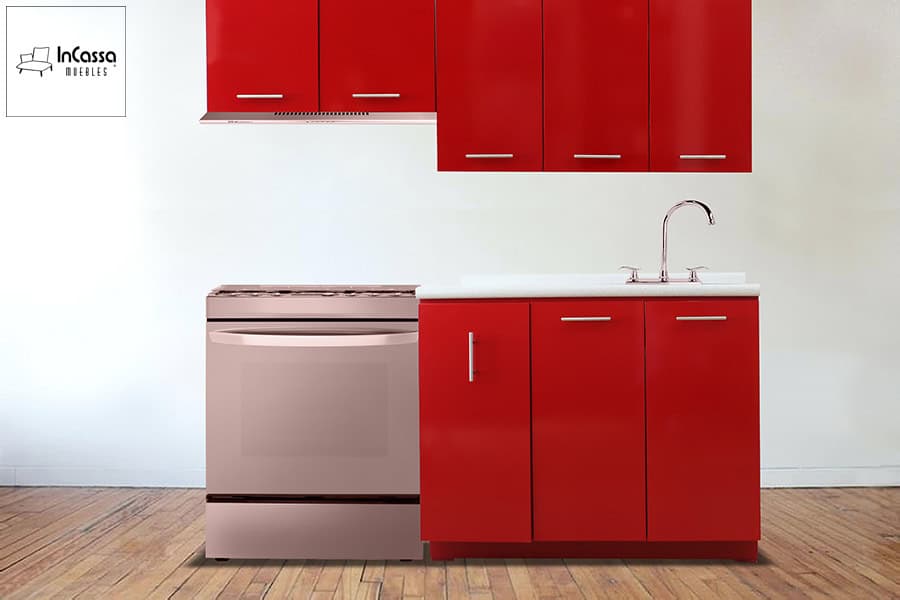 La imagen presenta una cocina integral color rojo vivo brillante en toma frontal completa. Destaca la distribución lineal con tarja de acero, cubierta de formaica estilo sal y pimienta y estufa metálica al centro. El fondo blanco y el piso tipo madera realzan el contraste del mobiliario.