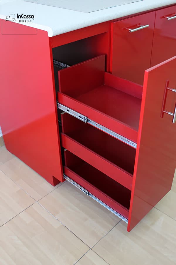 La imagen muestra un acercamiento lateral del especiero inferior con sus tres niveles de almacenamiento completamente extendidos. El acabado rojo vivo contrasta con los rieles metálicos, resaltando su diseño práctico y moderno bajo la cubierta de formaica sal y pimienta.