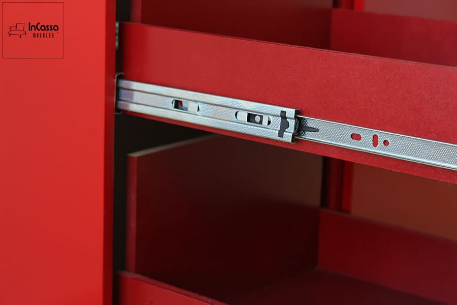 La toma muestra un primer plano de la corredera metálica instalada en el especiero extraíble. El acabado cromado resalta sobre el MDF en rojo vivo, evidenciando la calidad de los herrajes y el sistema de rieles de extensión suave que garantiza un deslizamiento firme y silencioso.