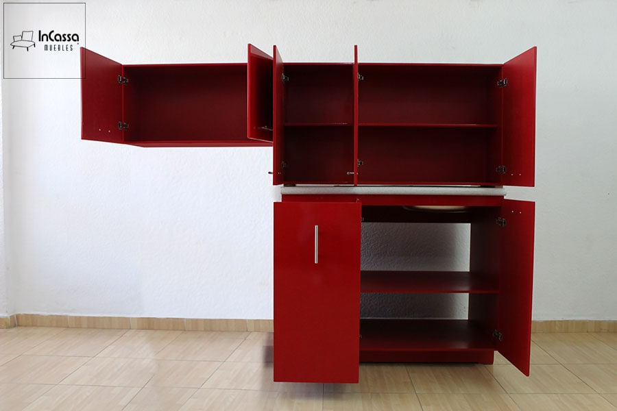 Se presenta una toma frontal de la cocina en color rojo vivo, mostrando todos los módulos con puertas abiertas. La imagen revela la capacidad interior de alacenas y gabinetes, con estantes funcionales para optimizar el almacenamiento. El fondo claro permite apreciar mejor el contraste.