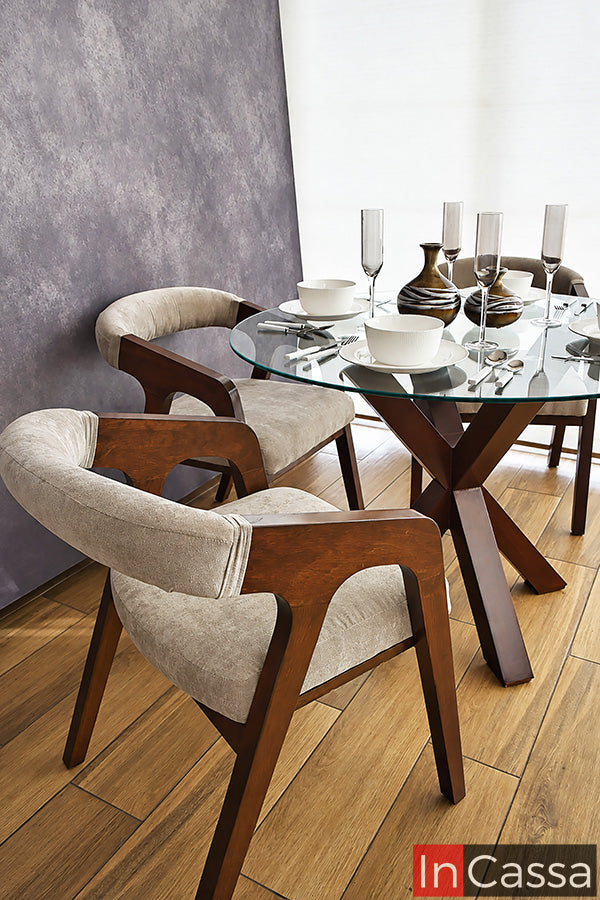 Desde un ángulo lateral, el Comedor Redondo Viral en Pinterest FORMENTERA con Mesa de Vidrio destaca por su estructura en color tabaco y sillas tapizadas en suede gris perla. La toma permite apreciar el diseño envolvente de los respaldos, los descansabrazos y la base geométrica de la mesa.