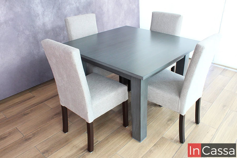 En esta imagen se observa el comedor cuadrado de cuatro sillas, con una mesa en tono gris cenizo oscuro y sillas tapizadas en pliana gris perla. La combinación de colores neutros crea un ambiente sereno y sofisticado.