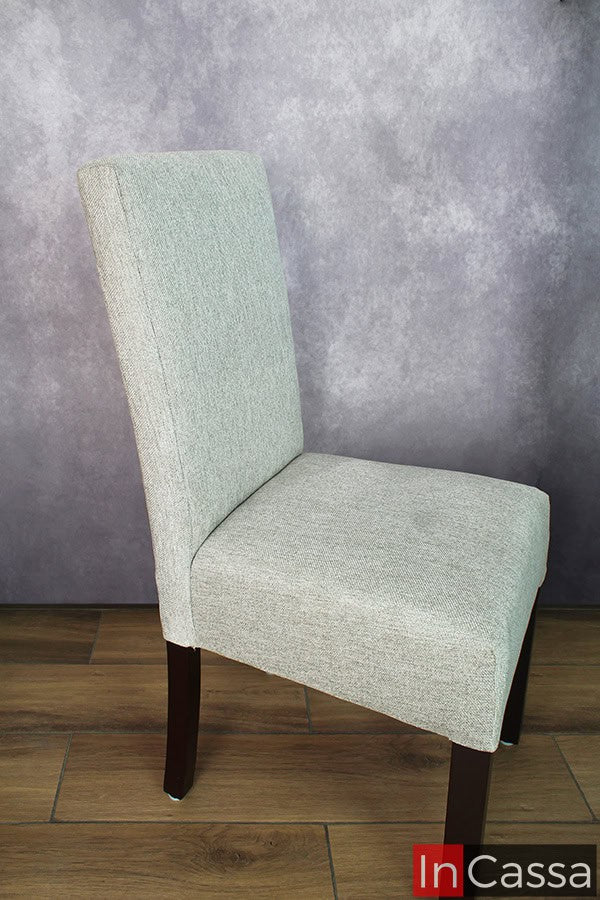 Se presenta una silla de estilo contemporáneo en tela pliana color gris perla, con un respaldo alto y patas de madera de pino oscura. Este diseño ofrece una mezcla de confort y elegancia para cualquier espacio.