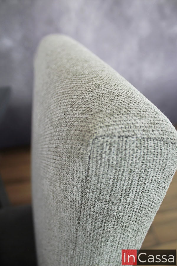 La imagen muestra un acercamiento al respaldo de la silla tapizada en tela pliana color gris perla, destacando la textura suave y resistente del material, ideal para un comedor elegante y moderno.